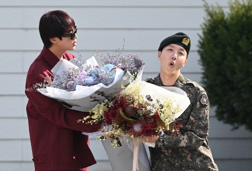 Mengenakan seragam dan baret hitam, J-Hope tersenyum saat menyapa Jin dan sekitar 100 penggemar yang bersorak serta wartawan saat keluar dari pangkalan militer di Wonju, Provinsi Gangwon. 