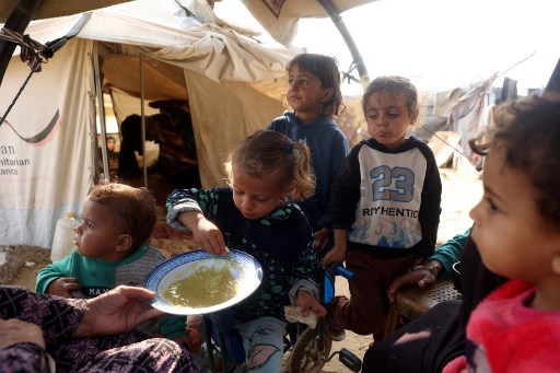 Seorang wanita Palestina yang telantar memberi makan anak-anaknya roti yang dicelupkan ke sup miju-miju di depan tenda di kamp pengungsi Al-Bureij di Jalur Gaza Tengah, Minggu, 10 November 2024.