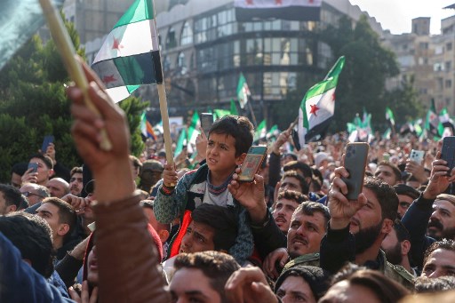 Pada hari Rabu, pejuang pemberontak mengibarkan bendera mereka saat berdiri di atas makam Hafez al-Assad yang hangus dan hancur, yang diwarisi kekuasaan oleh Bashar al-Assad.