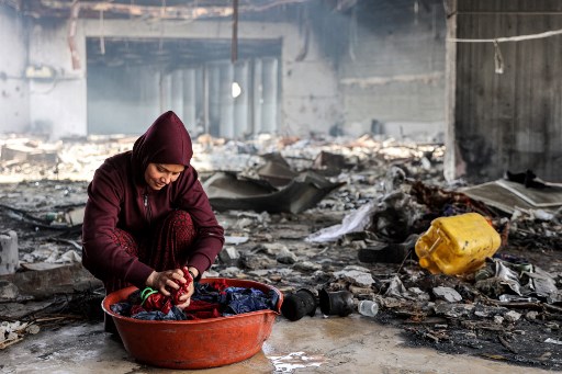 Seorang perempuan pengungsi dari Jabalia mencuci pakaian dengan tangan di baskom di samping puing-puing di Pusat Kebudayaan Rashad al-Shawa yang rusak parah akibat pemboman Israel di Kotamadya Gaza.