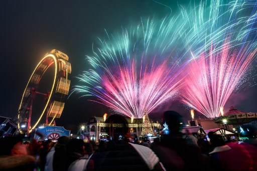 Orang-orang menyaksikan kembang api yang menerangi langit Wina, Austria, tepat setelah tengah malam pada 1 Januari 2025. AFP PHOTO/Max Slovencik