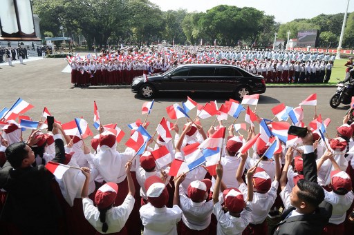 Para pelajar dengan antusias mengibarkan bendera Indonesia dan Prancis, yang menambah semarak suasana penyambutan iring-iringan kendaraan Presiden Macron.