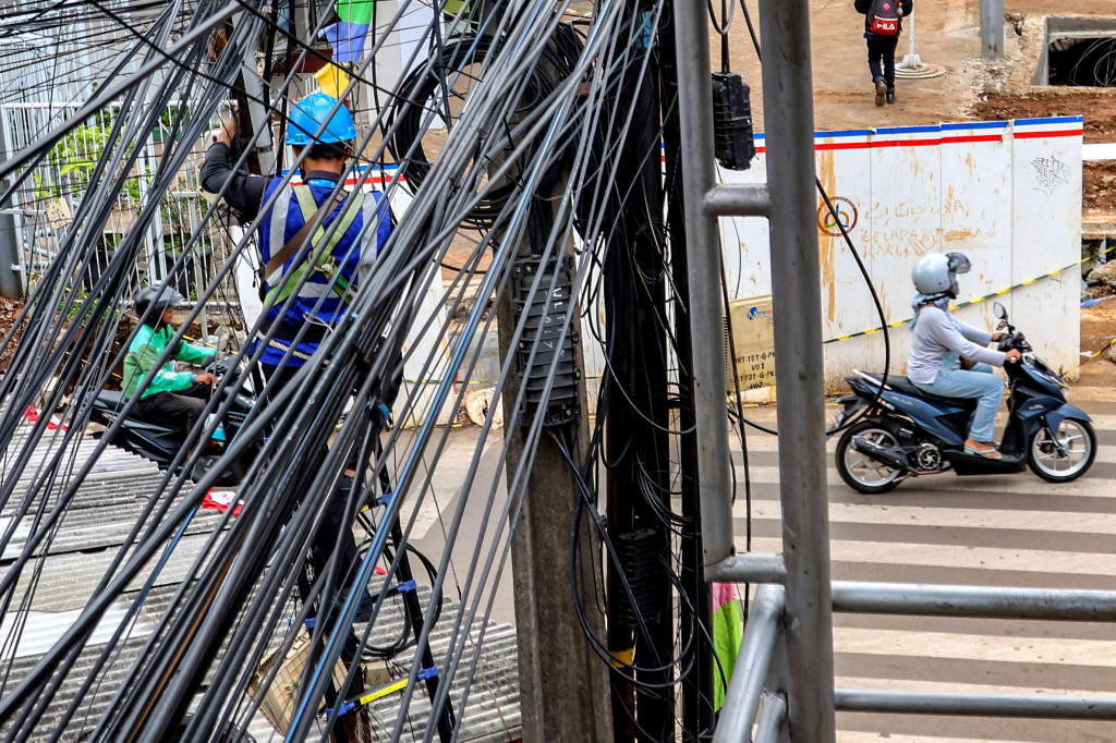 Seorang pekerja terlihat sedang melakukan perbaikan pada instalasi jaringan kabel udara yang tampak semrawut di kawasan Jalan Saharjo, Jakarta Selatan, Kamis, 14 Agustus 2025. 