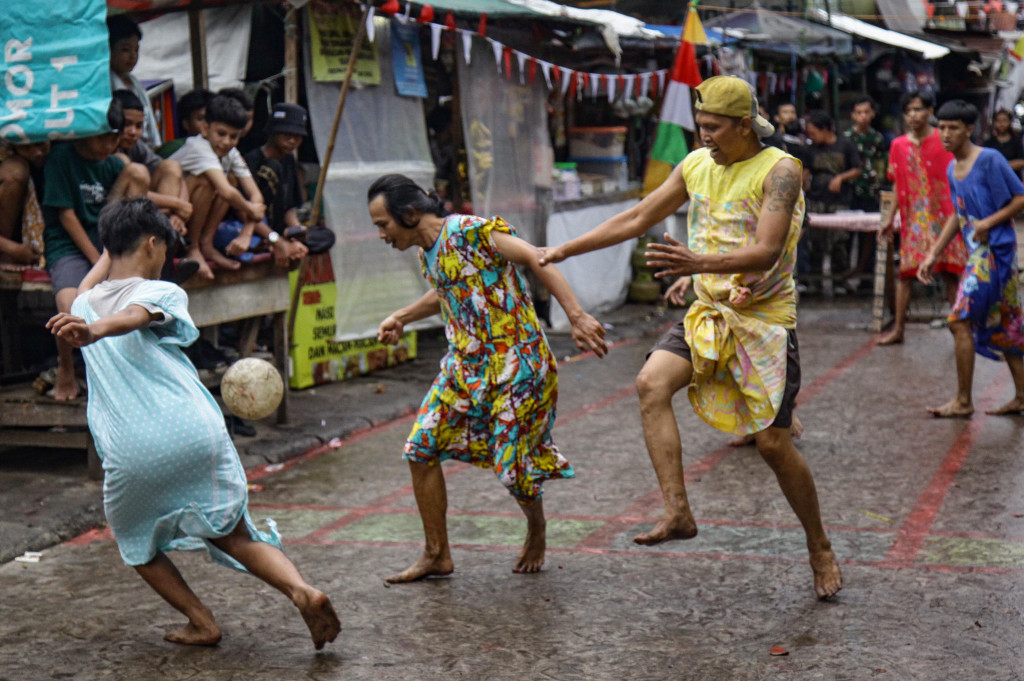 Para peserta pria dengan penuh semangat mengenakan daster dan mencoba mencetak gol ke gawang, memancing gelak tawa penonton. 