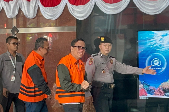 Status tersangka itu terlihat karena Noel menggunakan rompi oranye khas tahanan KPK. Penyidik dan tim pengamanan juga memborgol tangannya.