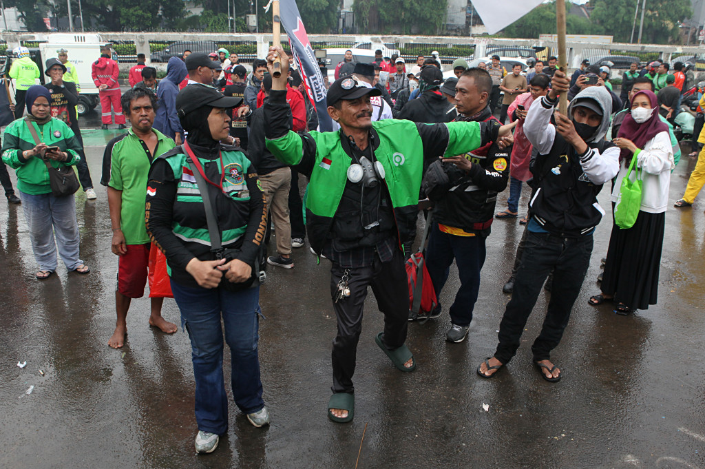 Puluhan pengemudi ojek daring/online (ojol) menerobos hujan deras untuk berunjuk rasa di depan Gedung DPR/MPR untuk menyampaikan sejumlah aspirasi seperti potongan komisi di aplikasi maksimal 10 persen.
