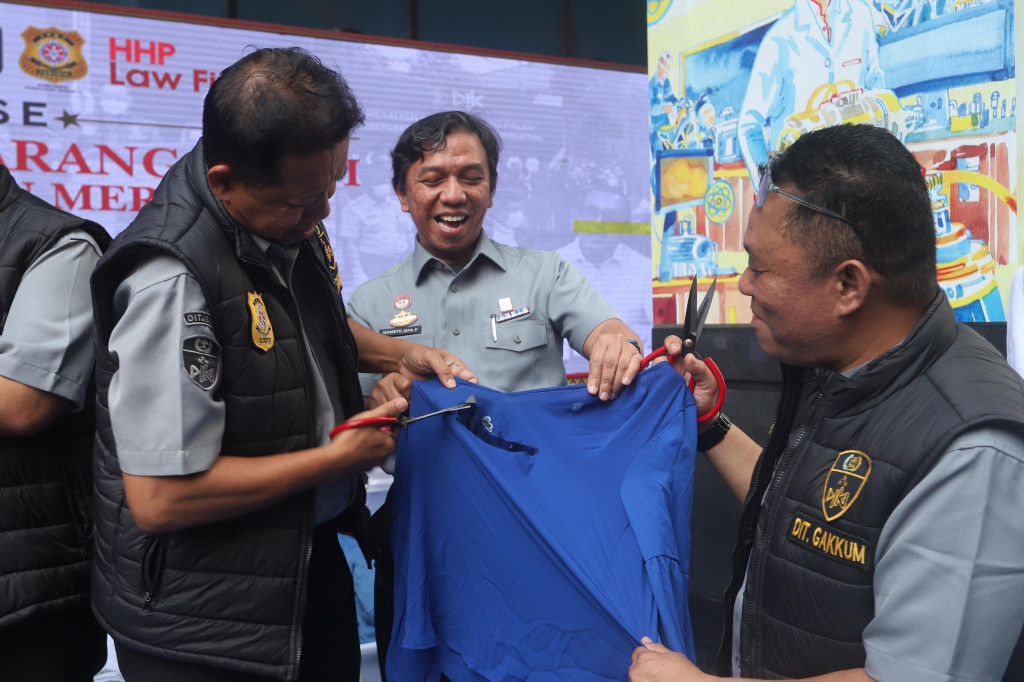 Petugas Dit Gakkum Kementerian Hukum, menggunting pakaian bermerk Lacoste tiruan di Jakarta, Senin, 22 Juni 2026. 
