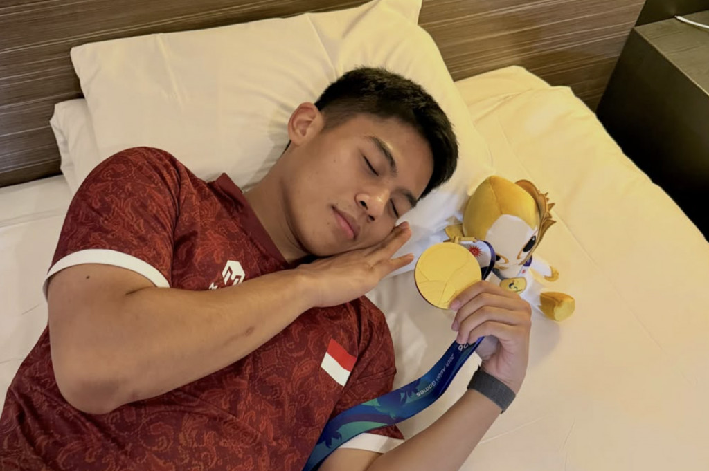 Dalam foto yang diunggah melalui media sosial pribadinya, Ubed tampak tertidur di atas tempat tidur sambil menggenggam erat medali emas yang baru diraihnya.
