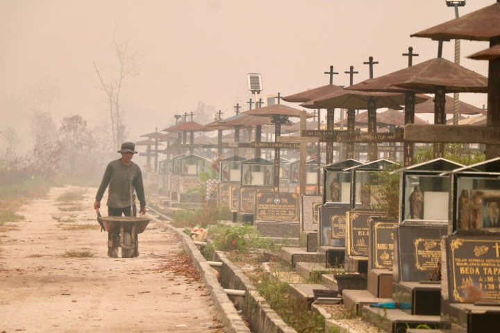 Seorang pekerja mendorong gerobak melewati area pemakaman umum yang diselimuti kabut asap tebal akibat kebakaran hutan dan lahan di Palangka Raya, Kalimantan Tengah, Rabu, 30 September 2026.